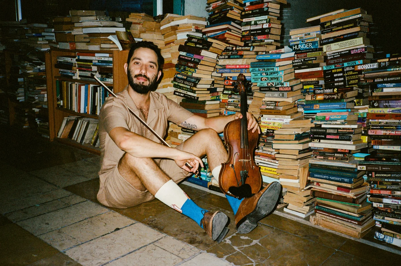 Omer, AltGarden's founder, sitting with a violin among stacks of books